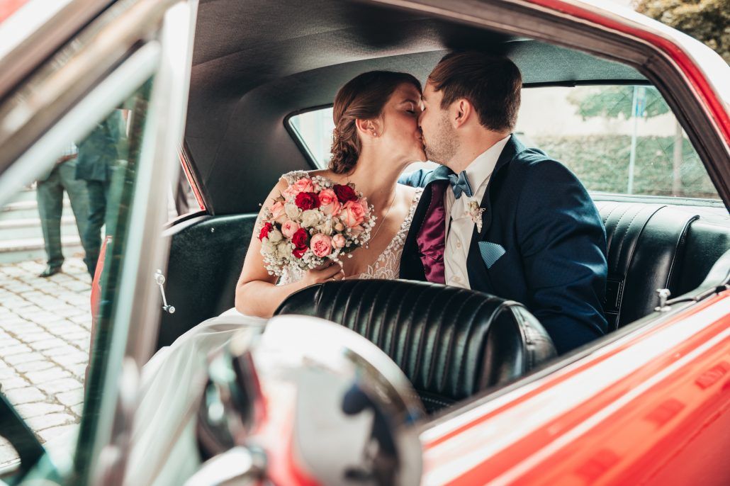 Brautpaar küsst sich auf der Rücksitzbank vom Brautauto