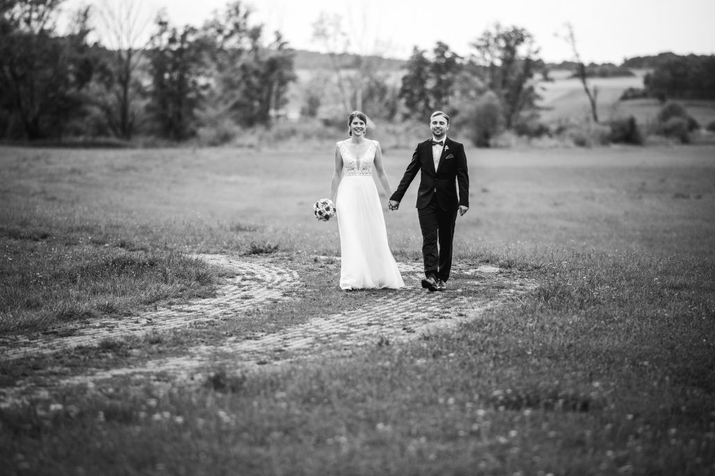 Brautpaar läuft auf einen Feldweg in die Richtung vom Fotograf
