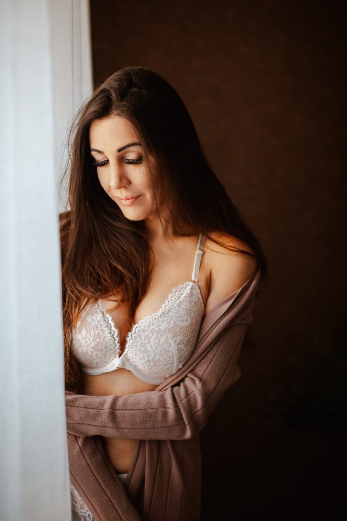 sensual Portrait einer Frau in Dessoussteht im Schlafzimmer am Fenster