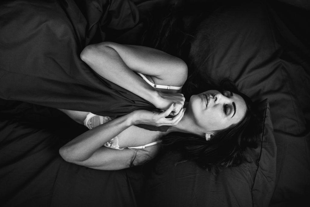 Sensual Portrait einer sexy Frau in Dessous liegt zugedeckt im Bett vom Fotograf