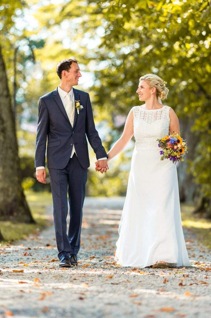Brautpaar läuft glücklich Hand in Hand beim Hochzeitsshooting den Fotograf entgegen