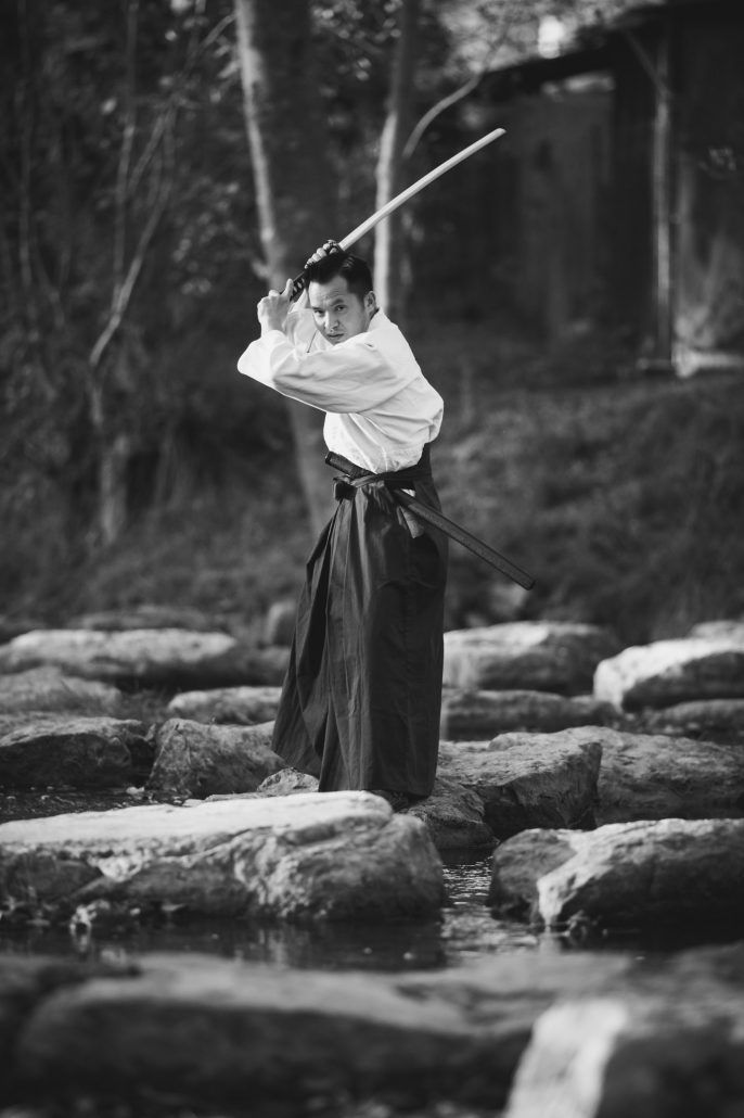 asiatischer Schwertkämpfer auf einen Stein im Fluss. Fotografiert in schwarz weiß