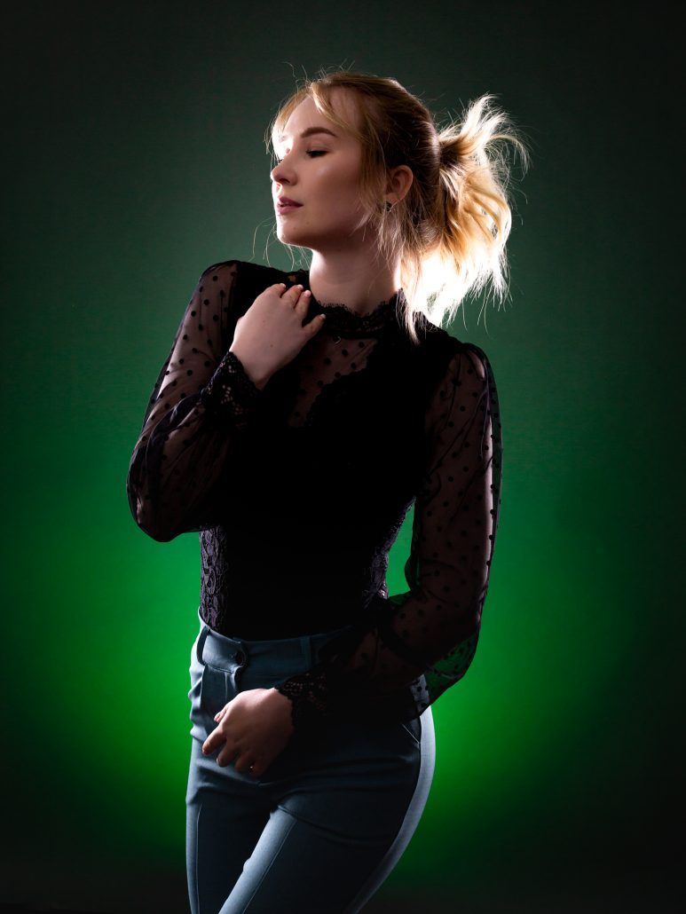 Portrait im Fotostudio einer Frau mit blonden Haaren vor grünen Hintergrund.