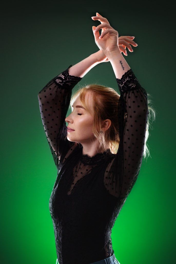 Studio Portrait einer Frau mit blonden Haaren vor grünen Hintergrund hat ihre Hände über den Kopf