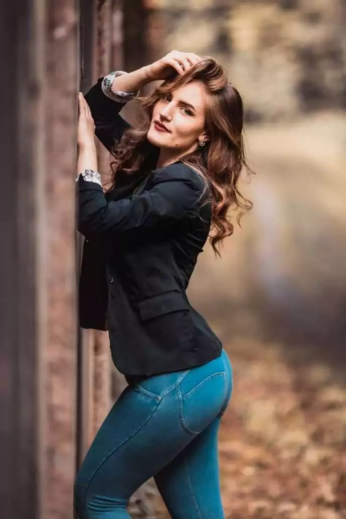 Frau mit langen braunen Haaren steht an einer Mauer und langt sich in ihre Haare - Foto vom Fotograf