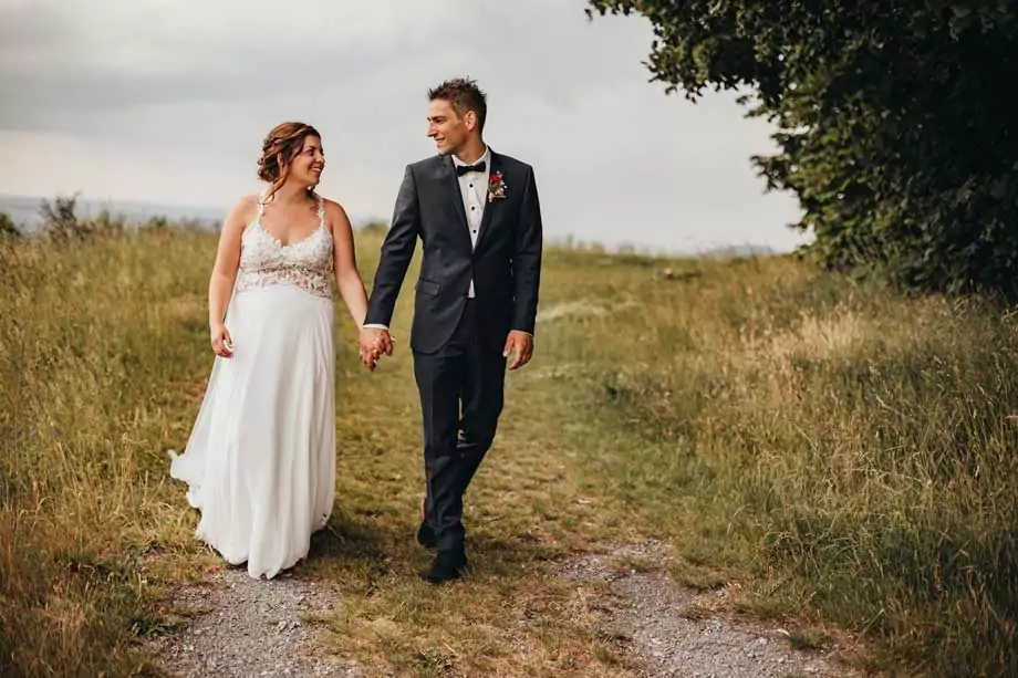 Brautpaar in Brautkleid und Anzug auf einem Naturpfad - romantisches Outdoor-Fotoshooting im Grünen mit Braut im weißen Kleid und Bräutigam im schwarzen Smoking