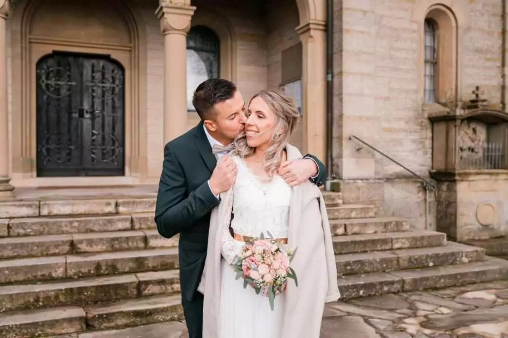 Brautpaar nach der Hochzeit vor der Kirche im Winter beim Brautpaarshooting